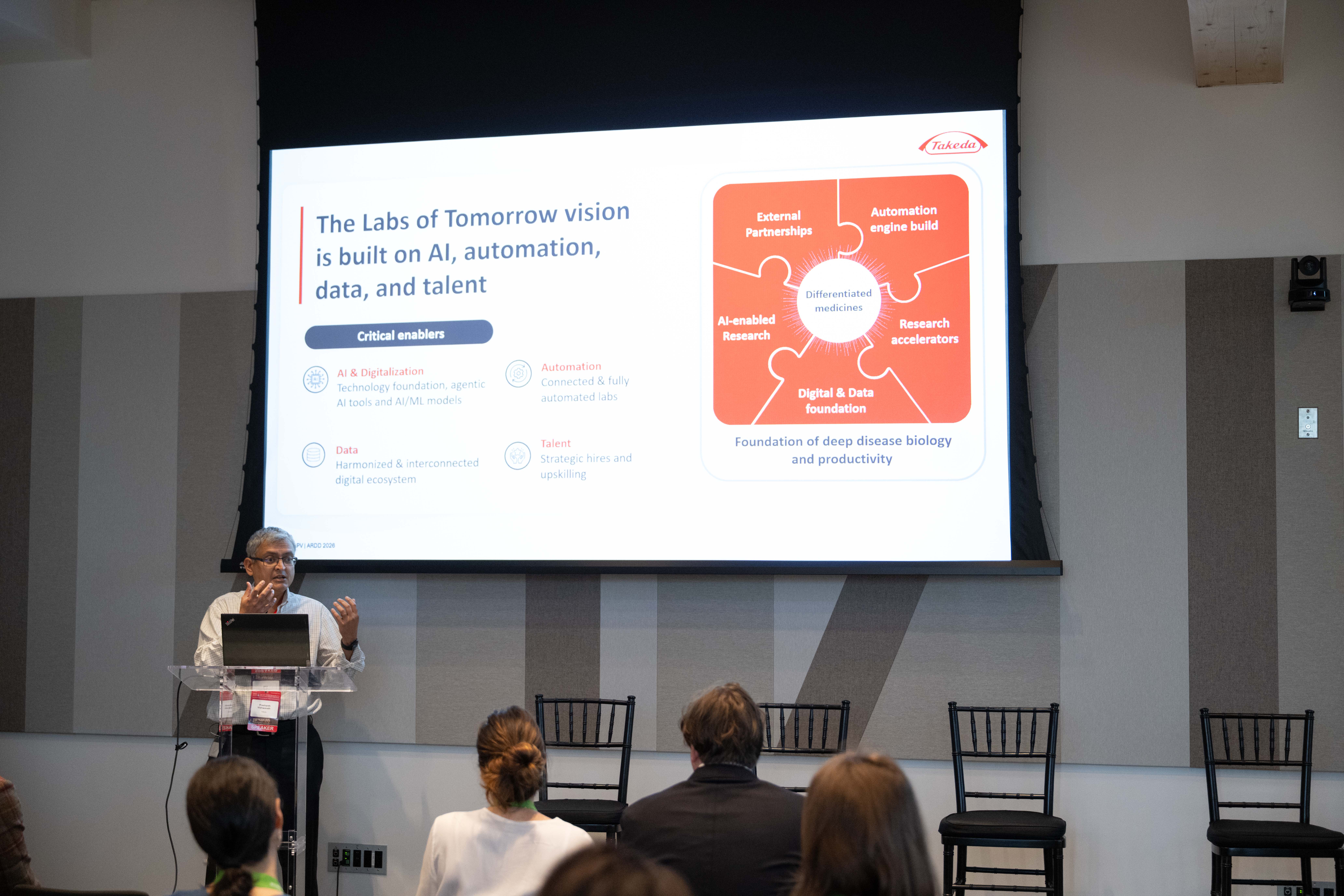 Prashanth Vishwanath at the forum podium beneath a Takeda slide about AI, automation, data and talent in the labs of tomorrow.