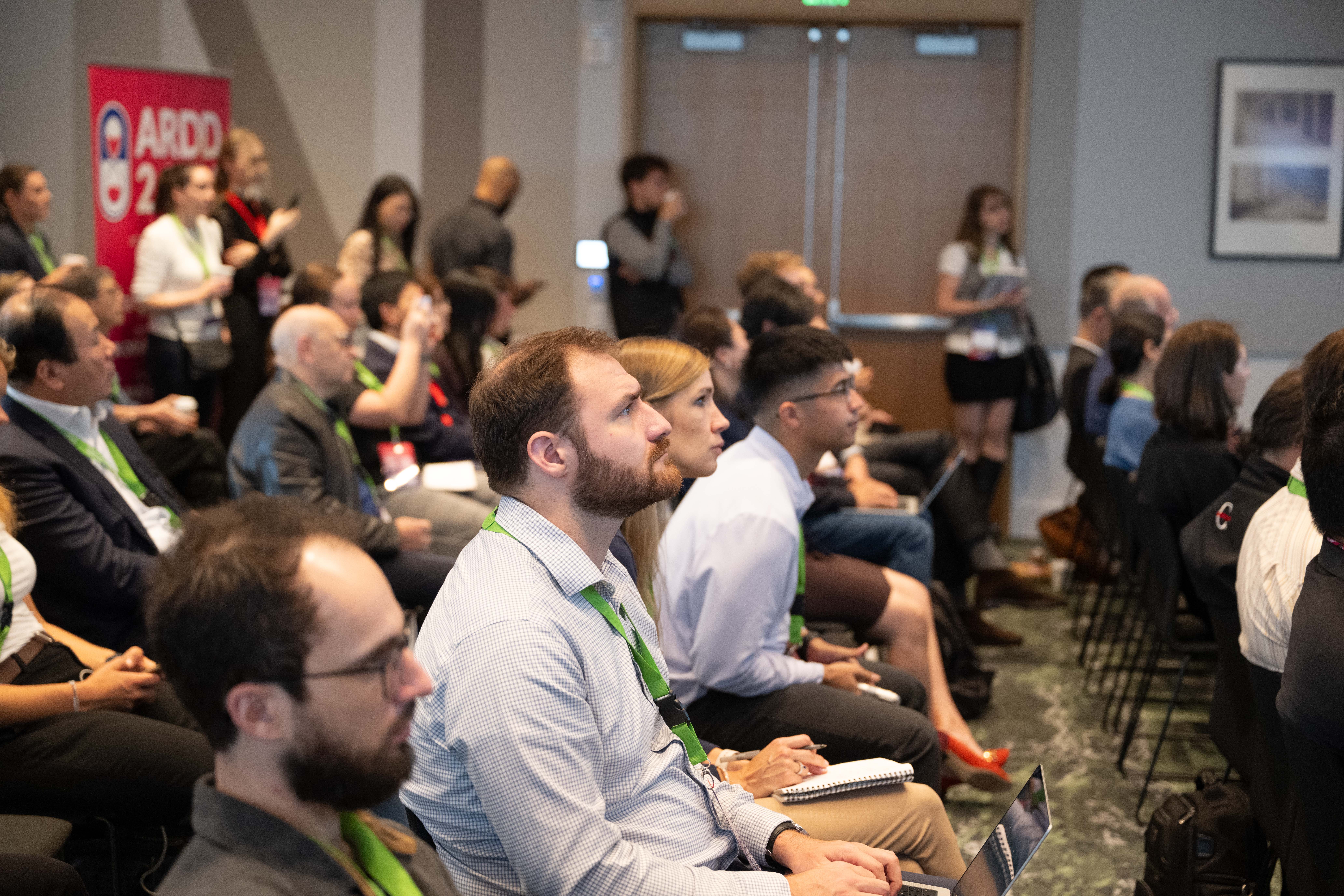 Audience members in the Cedar Grove forum room, with notebooks and cameras visible; no individual attendee is identified.